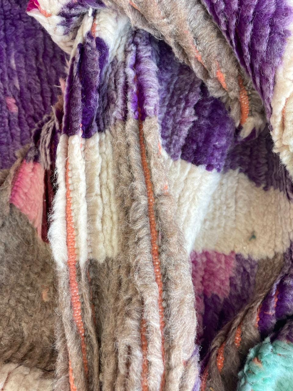Detail of a hand-woven purple rug with fringe edges and a textured surface.