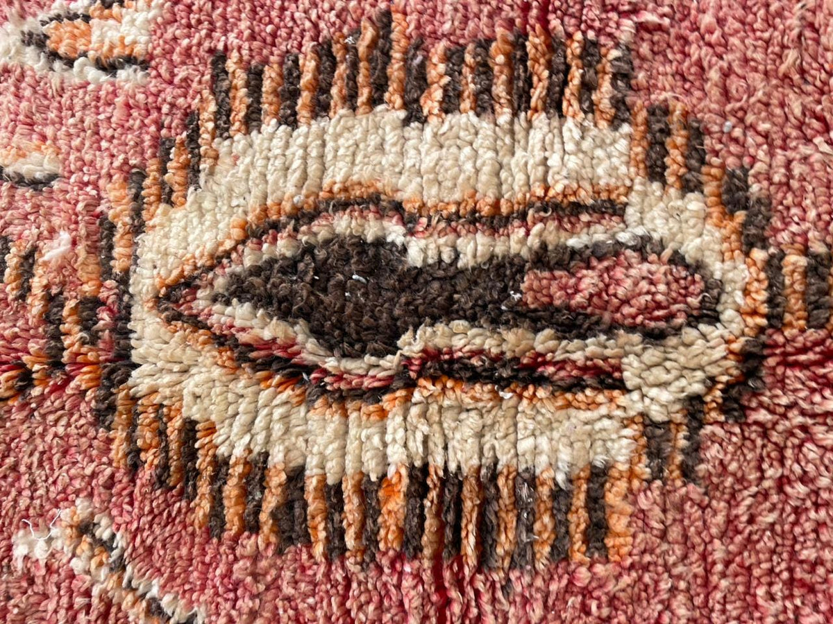 Close-up view of a vintage Moroccan rug featuring a tribal pattern in brown, red, and black.