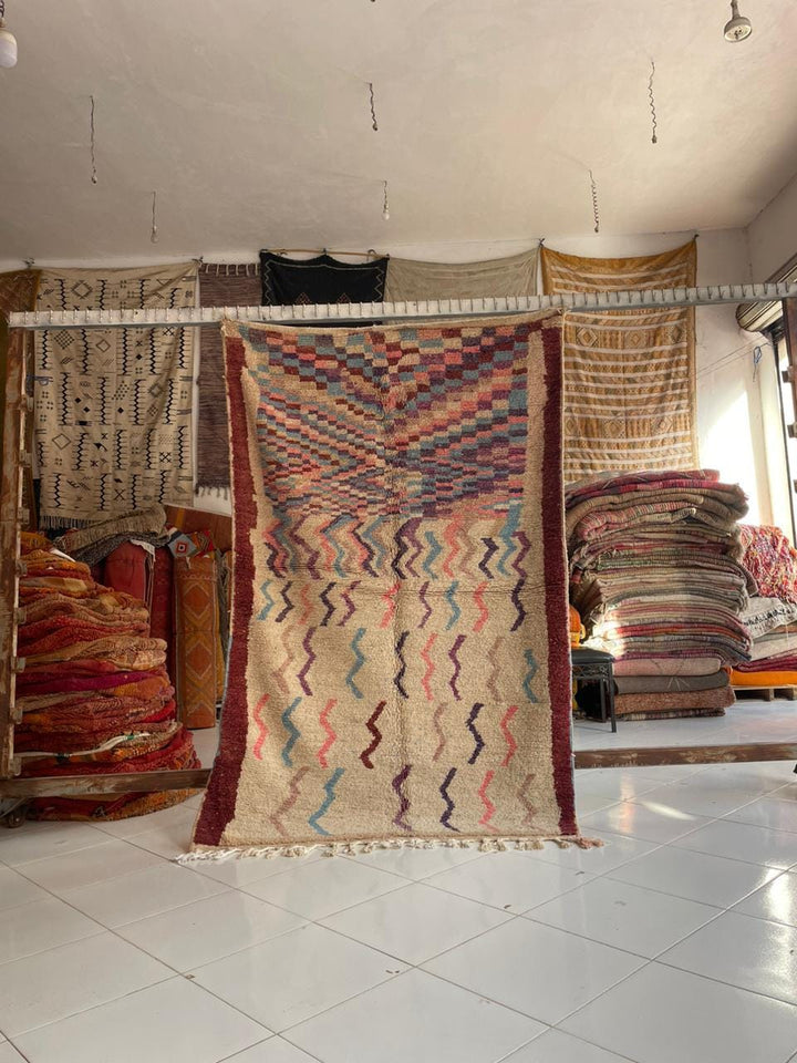 Lifestyle shot of a colorful Moroccan rug with red, beige, and blue hues in a natural setting.