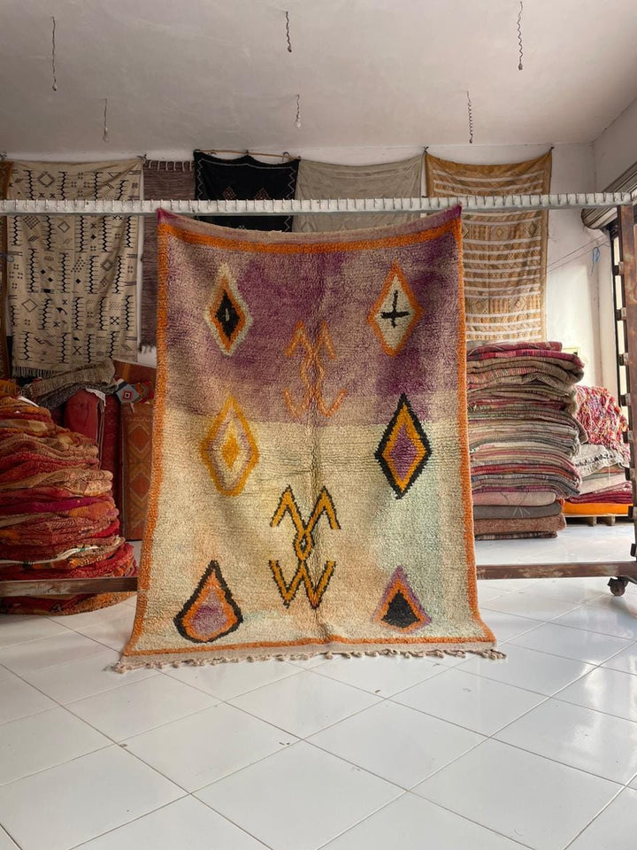 Lifestyle shot of a colorful Moroccan rug featuring geometric patterns and fringe edges.