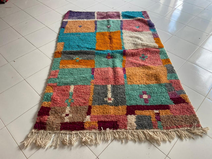 Lifestyle shot of a colorful Moroccan rug with orange, turquoise, and pink hues in a natural setting.