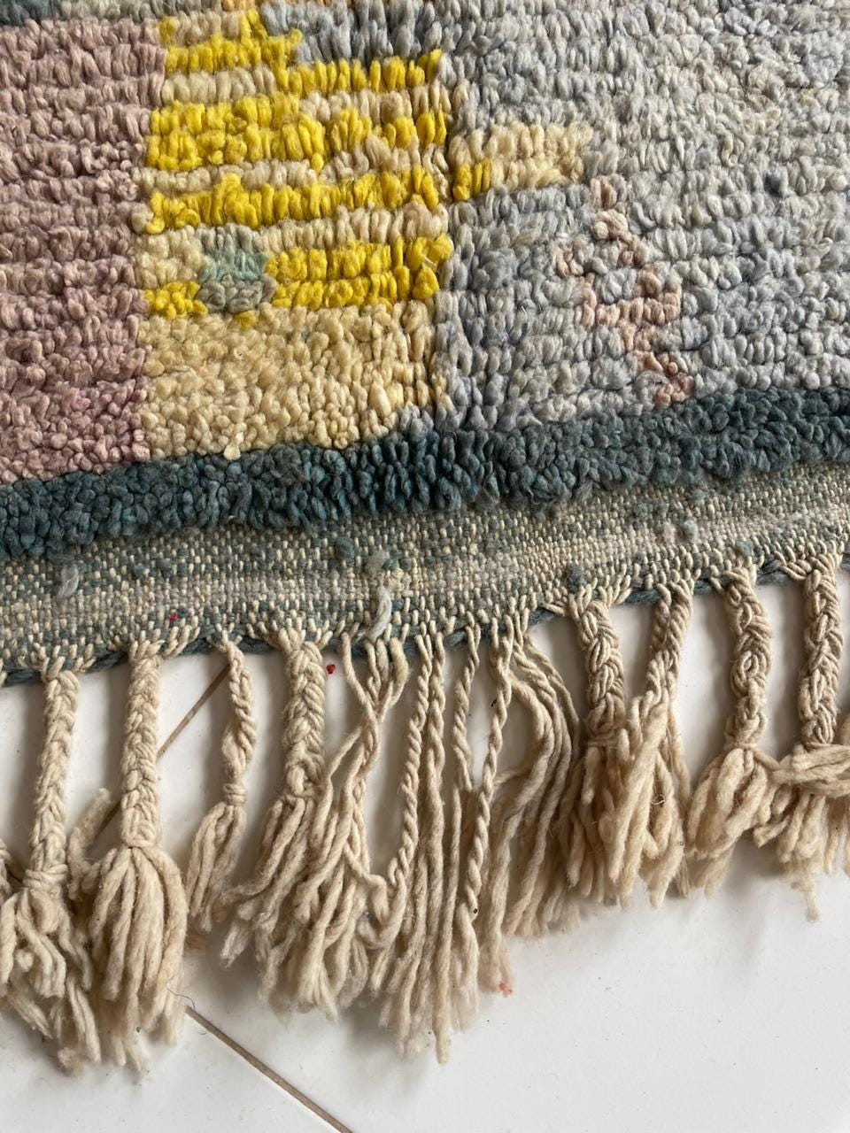Detail shot of a colorful rug with fringe edges and textured pattern against a white background.