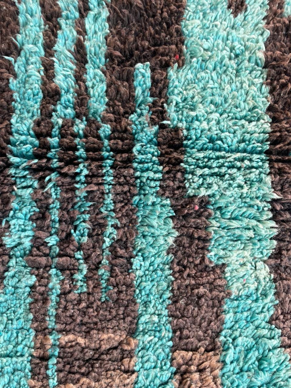 Detail of a colorful rug with a textured pattern in turquoise and brown.
