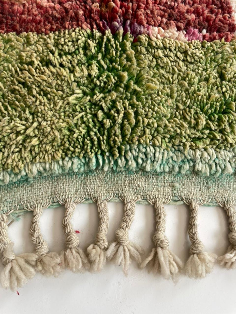 Close-up of a colorful rug featuring a textured weave in green, red, and cream.