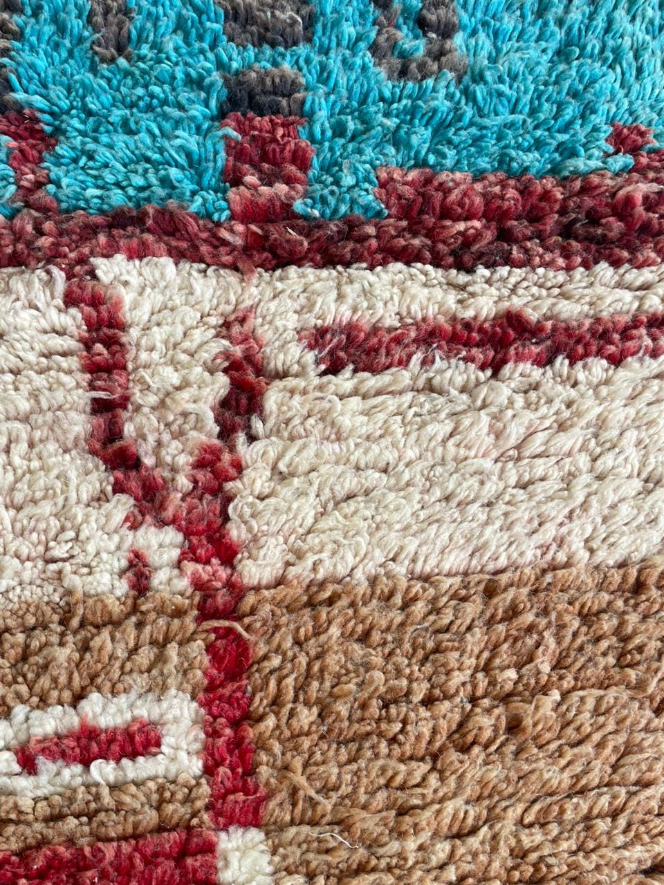 Close-up detail of the textured fibers and colorful patterns on the rug in brown, cream, red, and blue.