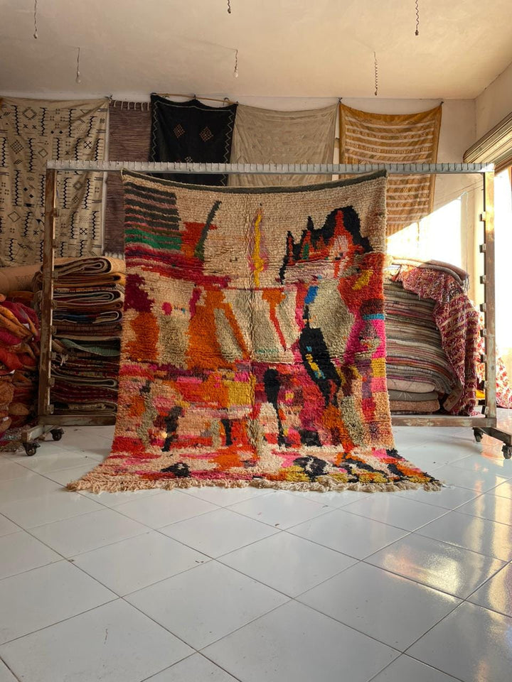 Lifestyle shot of a colorful Moroccan rug featuring orange, pink, and black colors with fringed edges.