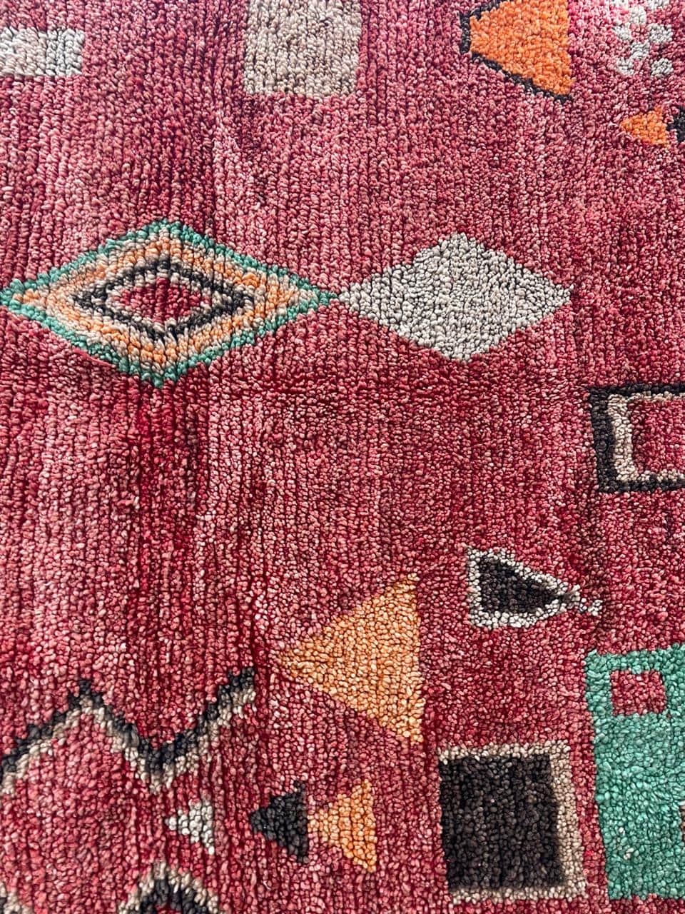 Close-up detail of a red Moroccan rug featuring fringed edges and colorful patterns.