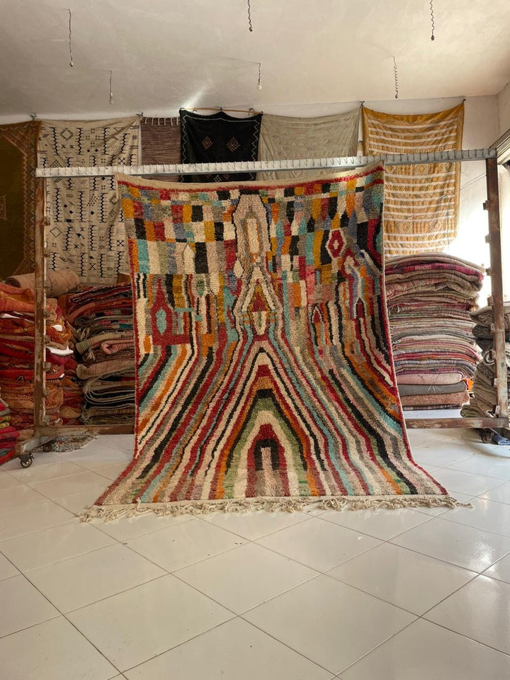Lifestyle shot of a colorful Moroccan rug featuring tribal patterns in red, orange, blue, and cream.