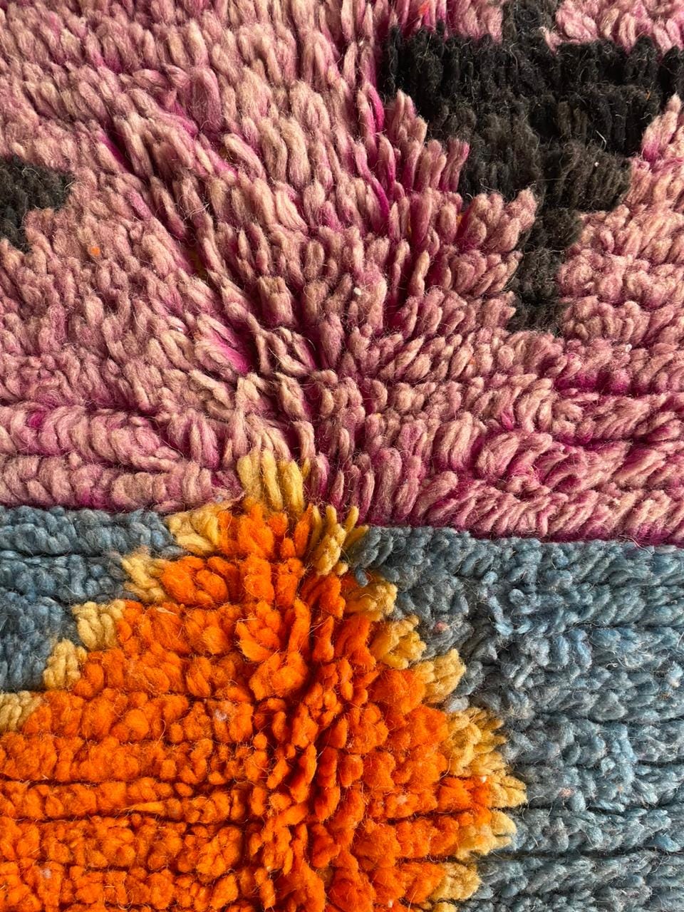Detail view of a colorful rug with a textured pattern in pink, orange, black, and blue.
