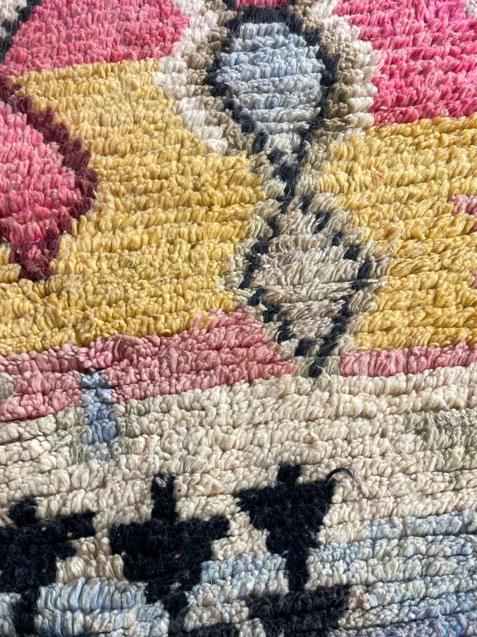Detail view of a colorful rug with diamond shapes and a textured surface.