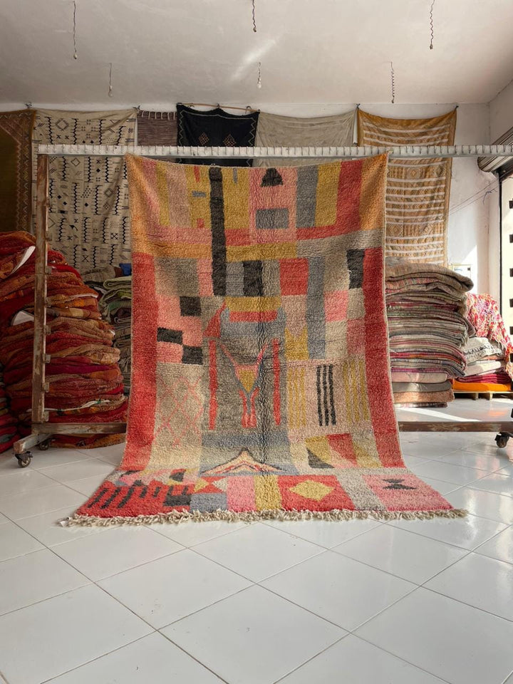 Lifestyle shot of a colorful Moroccan rug featuring geometric patterns and fringe edges.
