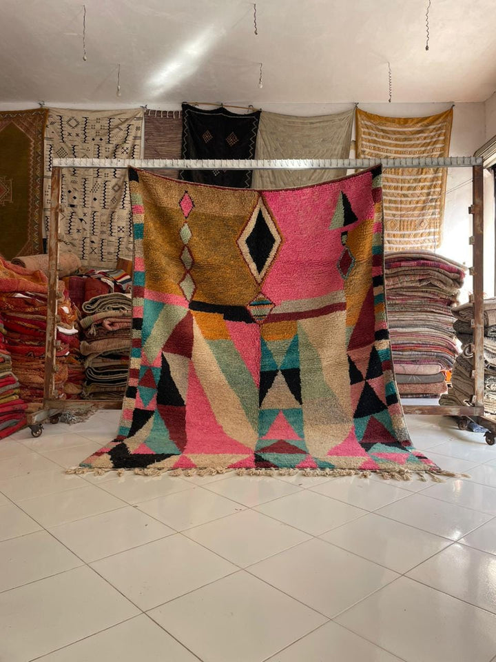 Lifestyle shot of a colorful Moroccan rug featuring geometric patterns and fringe edges.
