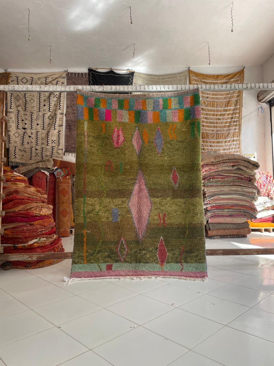 Lifestyle shot of a green Moroccan rug featuring tribal patterns and fringe edges.
