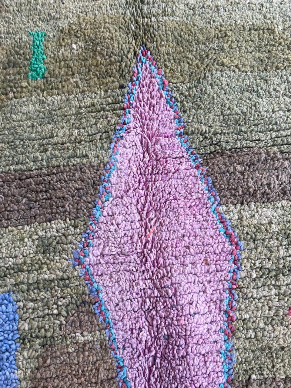 Detail close-up of a colorful rug pattern featuring a diamond shape and textured design.