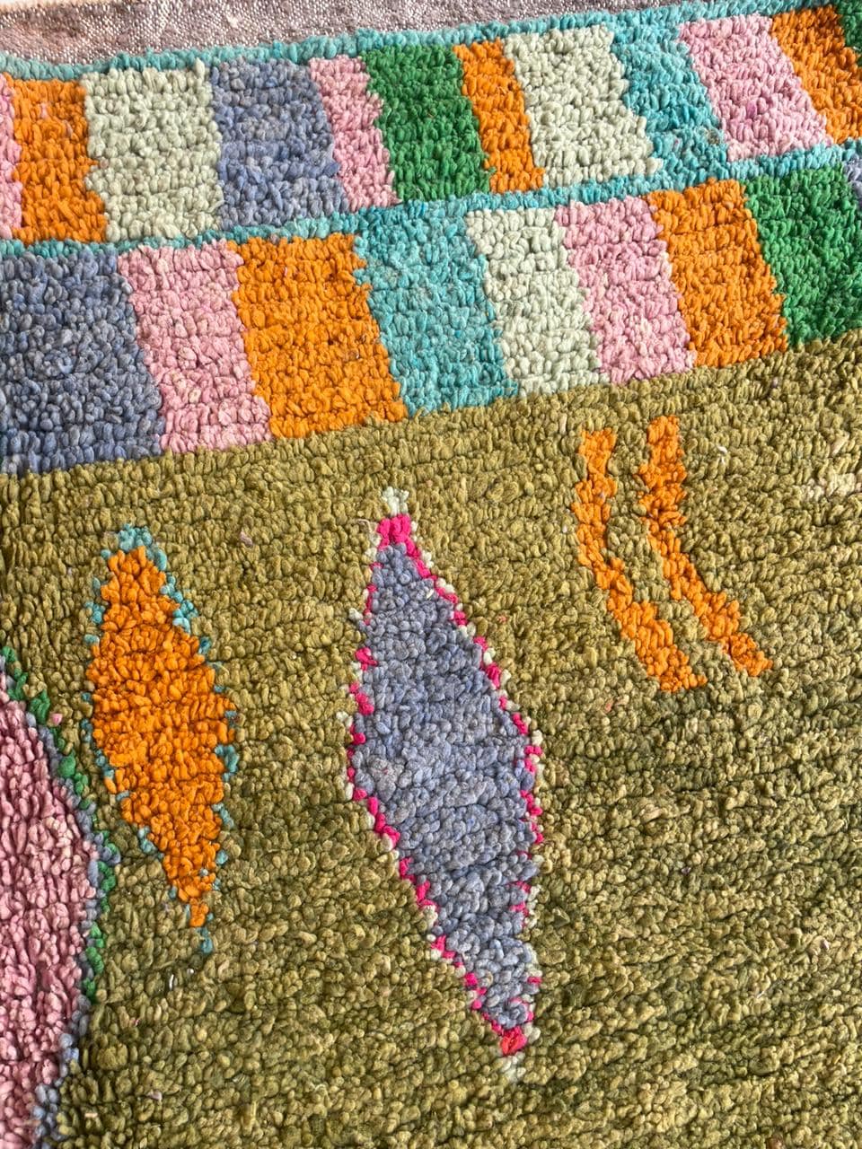 Detail close-up of a green Moroccan rug highlighting tribal patterns and fringe edges.