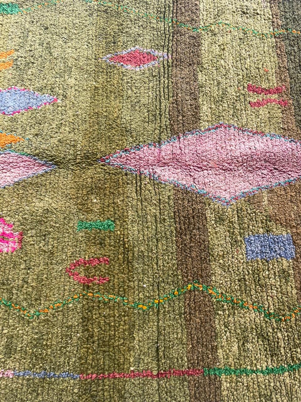 Detail close-up of a green Moroccan rug with colorful patterns and fringe edges.