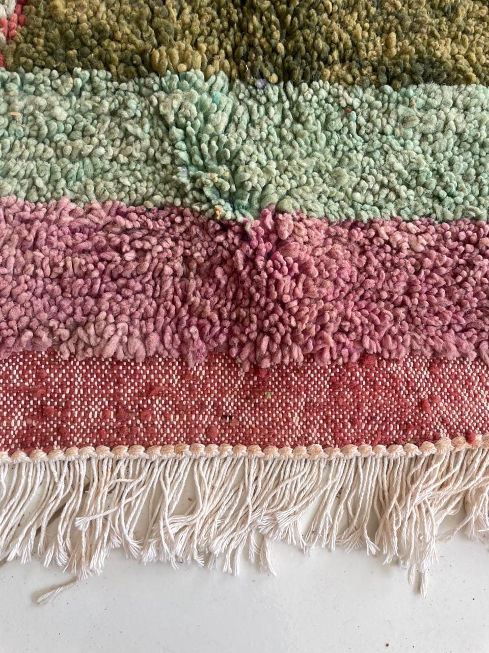 Detail close-up of a colorful rug edge with fringe and layered colors.