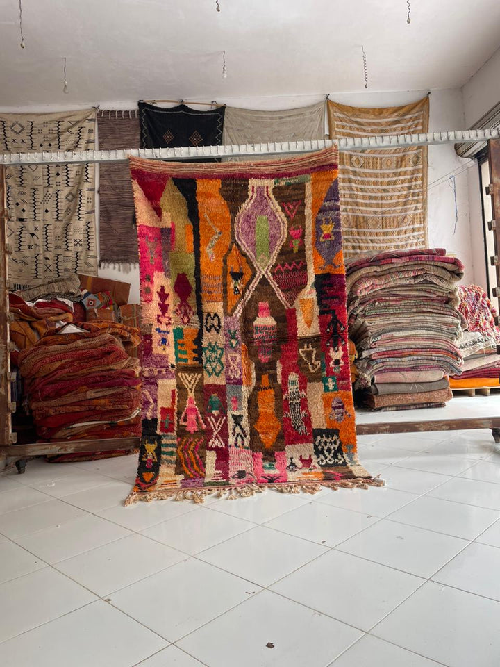 Lifestyle shot of a colorful Moroccan rug featuring geometric patterns and fringe edges.