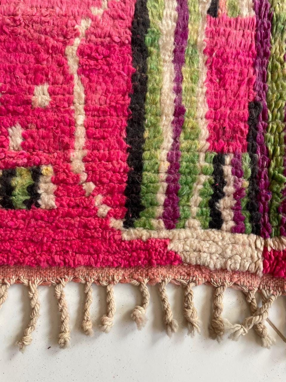 Close-up of a pink Moroccan rug with fringe edges and a striped pattern.