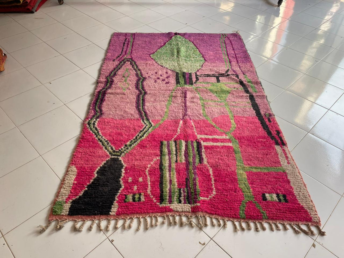 Top view of a pink Moroccan rug with fringed edges and geometric patterns.