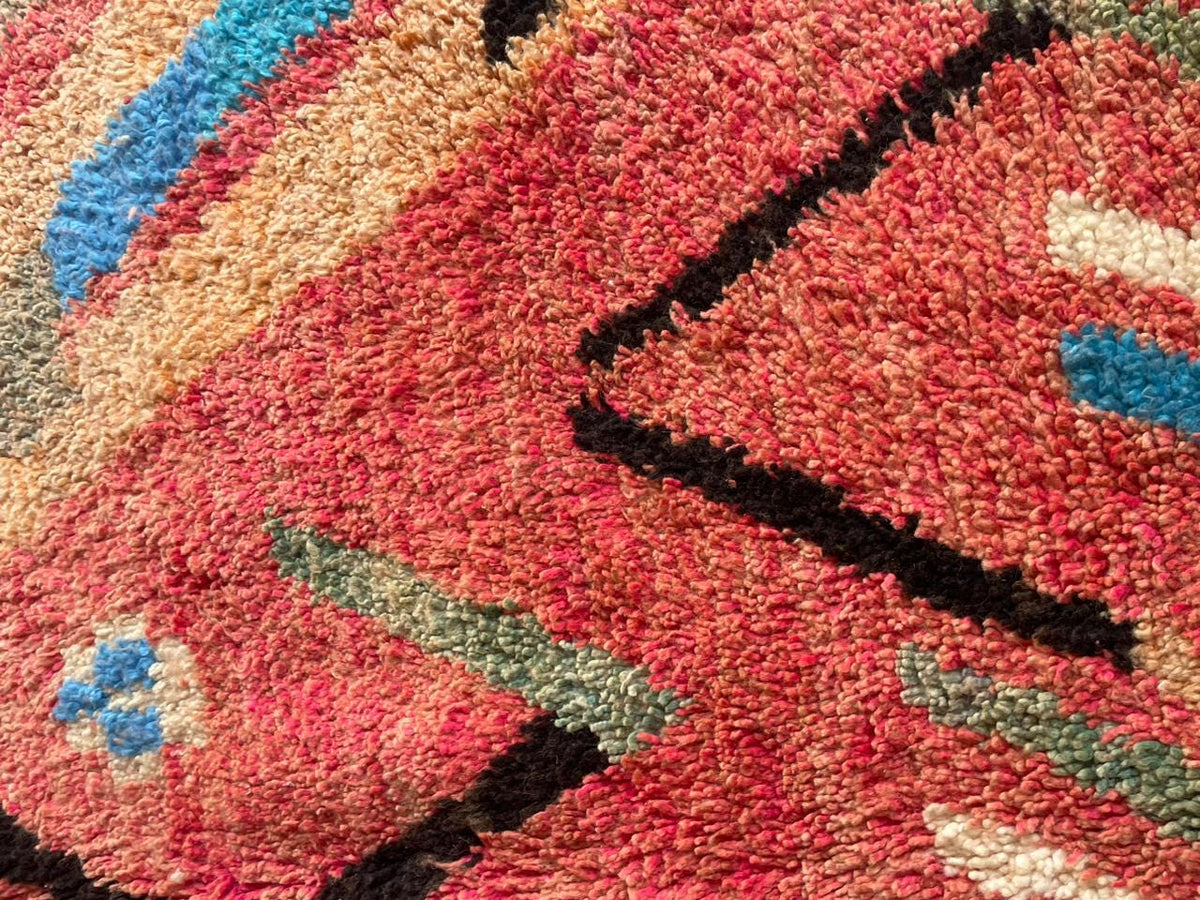 Close-up detail of a pink Moroccan rug with a colorful design and textured surface.