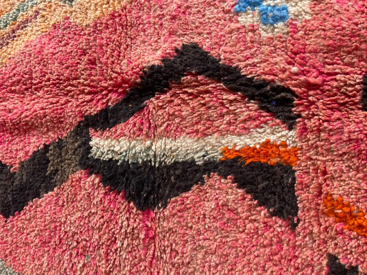 Close-up detail of a pink Moroccan rug featuring a geometric pattern and textured surface.