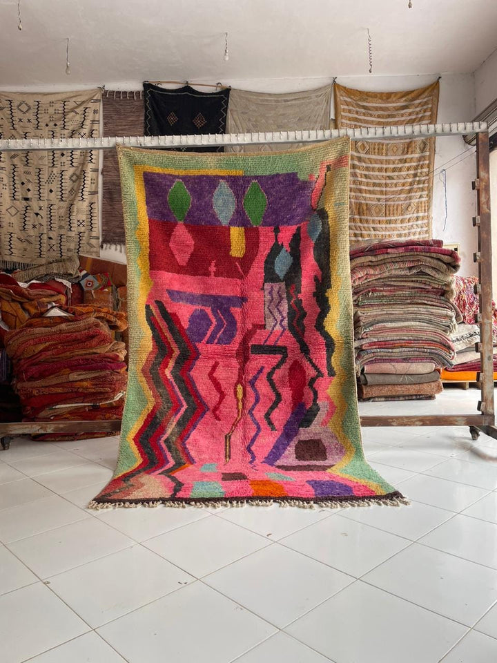 Lifestyle shot of a colorful pink Moroccan rug with abstract patterns and fringe edges.