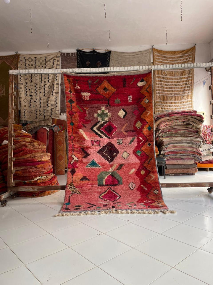 Lifestyle shot of the red and pink Boujaad Moroccan rug with geometric patterns on a natural background.
