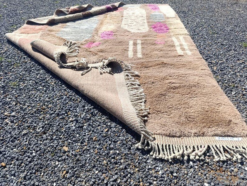 Detail view of the corner of a beige and pink abstract Moroccan rug with a textured surface.