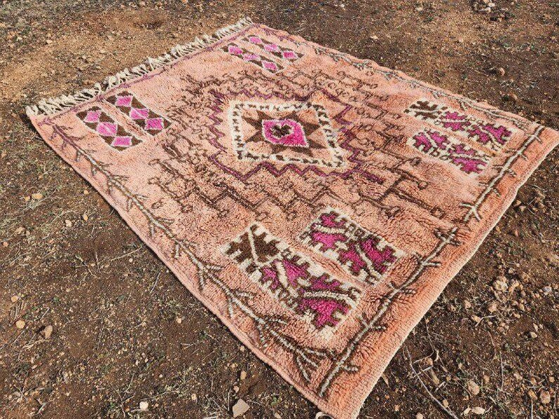 Close-up of a rust orange Moroccan rug with geometric patterns and fringed edges in a natural background.