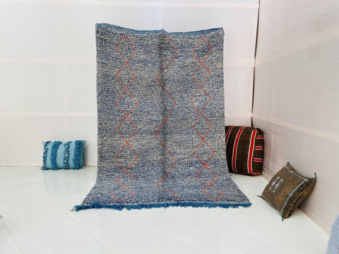 Lifestyle shot of a blue and red Beni Ourain Moroccan rug with abstract design on a white background.