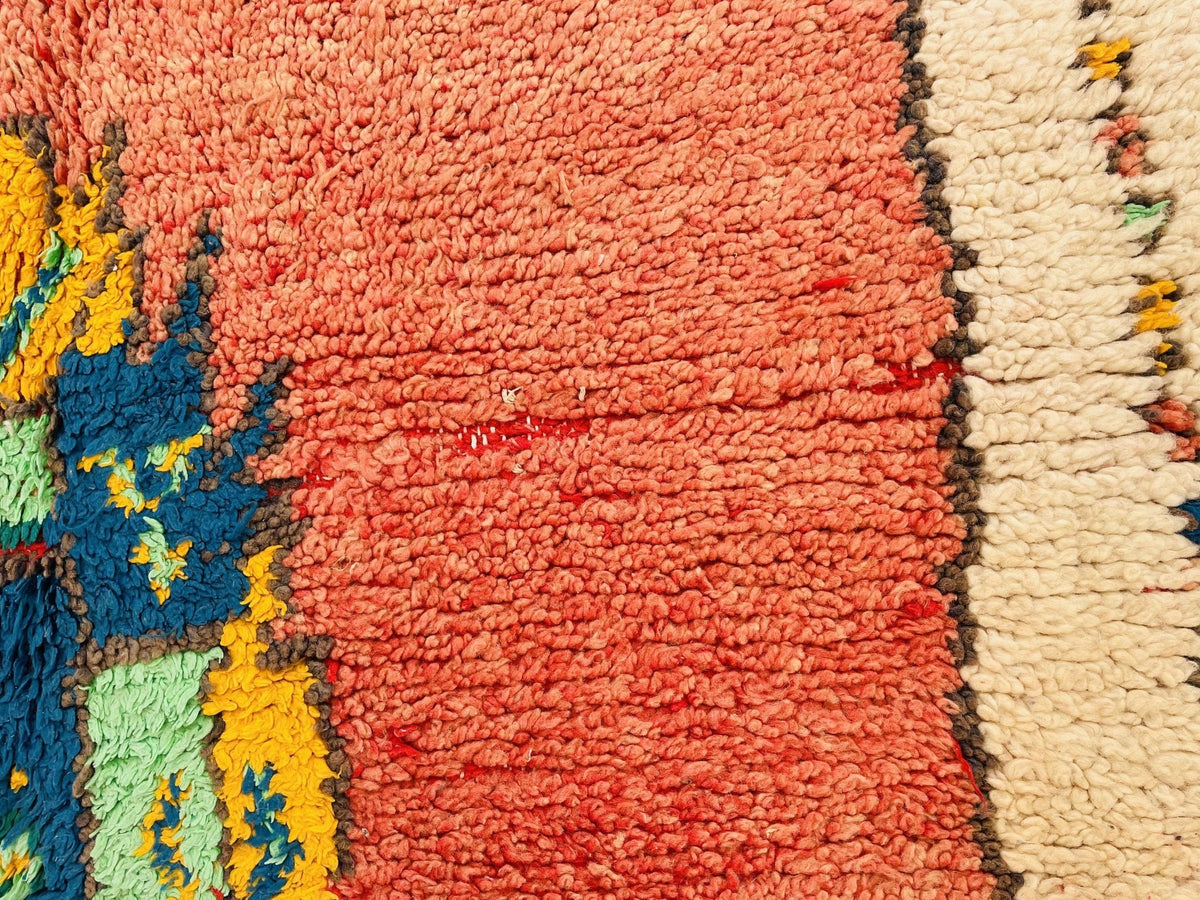 Close-up detail of the textured fabric of an orange Moroccan rug with colorful threads.