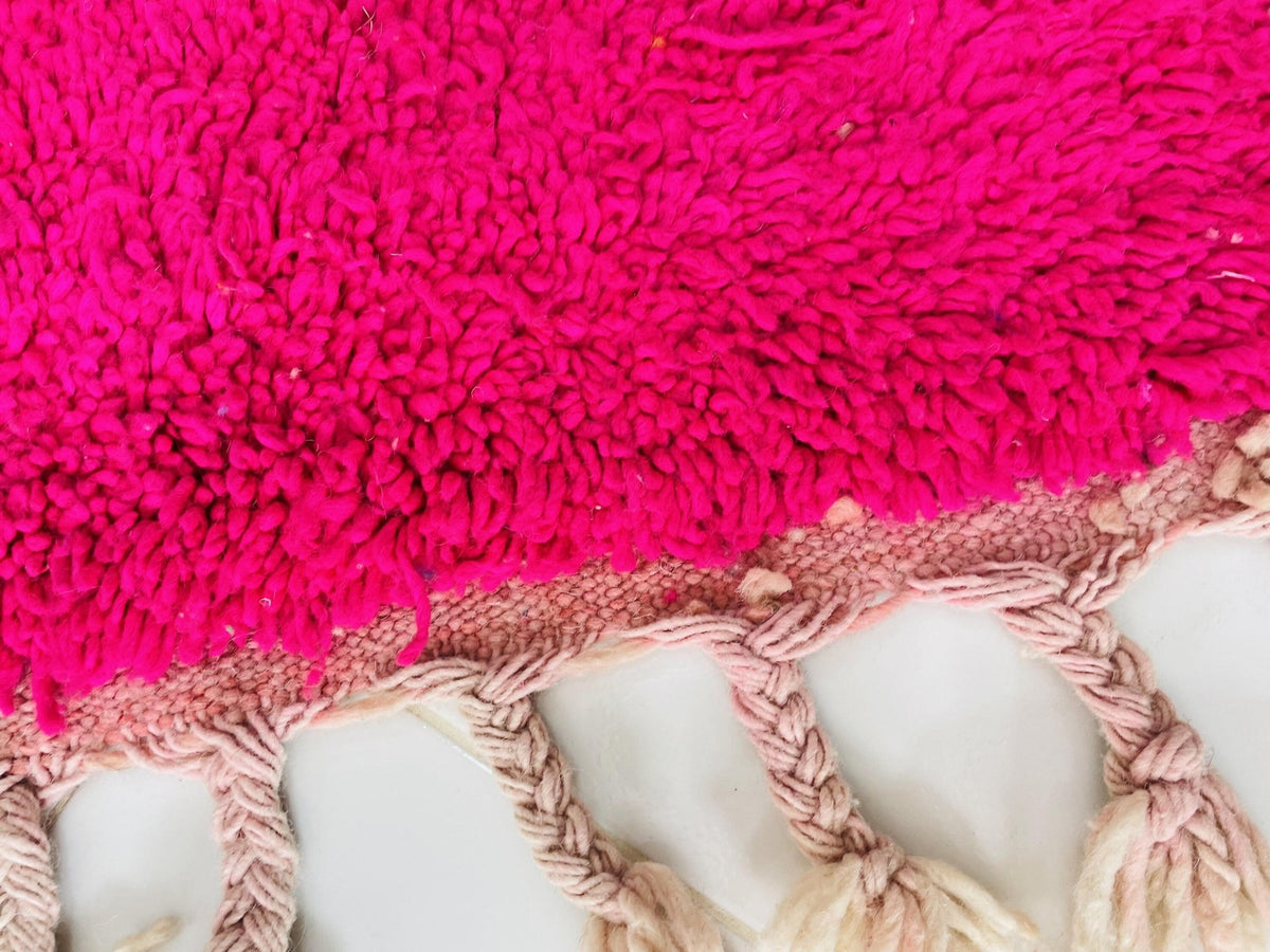 Close-up detail of the fringed edge and textured fibers of an orange and pink Moroccan rug.