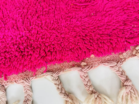 Close-up detail of the fringed edge and textured fibers of an orange and pink Moroccan rug.