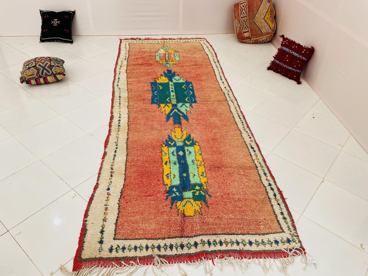 Lifestyle view of an orange Moroccan rug featuring geometric designs against a white backdrop.