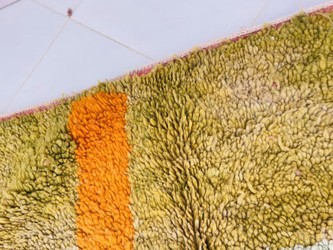 Close-up detail of a colorful orange and green Moroccan rug featuring a textured surface.