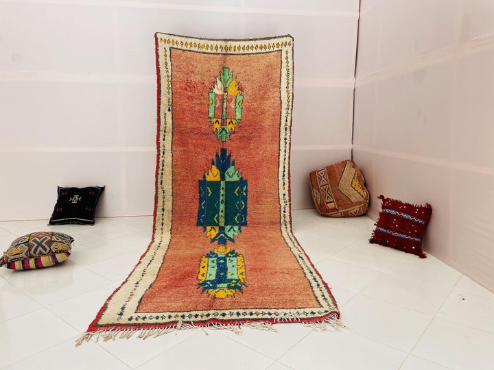Lifestyle shot of an orange Moroccan rug with geometric patterns on a white background.