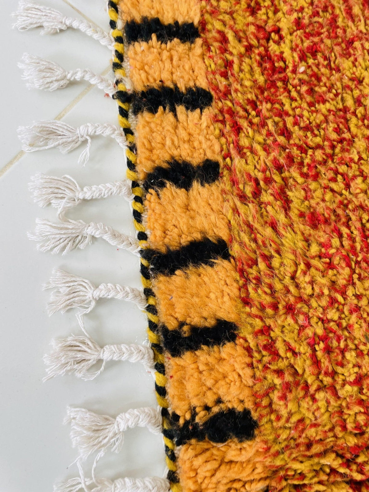 Close-up detail of the edge of an orange Moroccan rug highlighting fringe and color contrast.