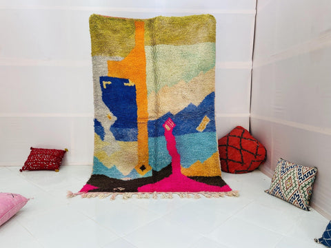 Lifestyle shot of a colorful orange and blue abstract Moroccan rug on a white background.