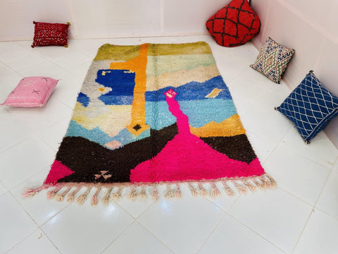 Lifestyle view of a vibrant orange and blue abstract Moroccan rug displayed on a white surface.