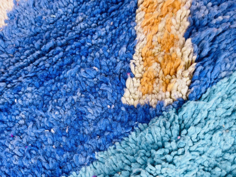 Close-up view of a colorful orange and blue Moroccan rug emphasizing its textured surface.