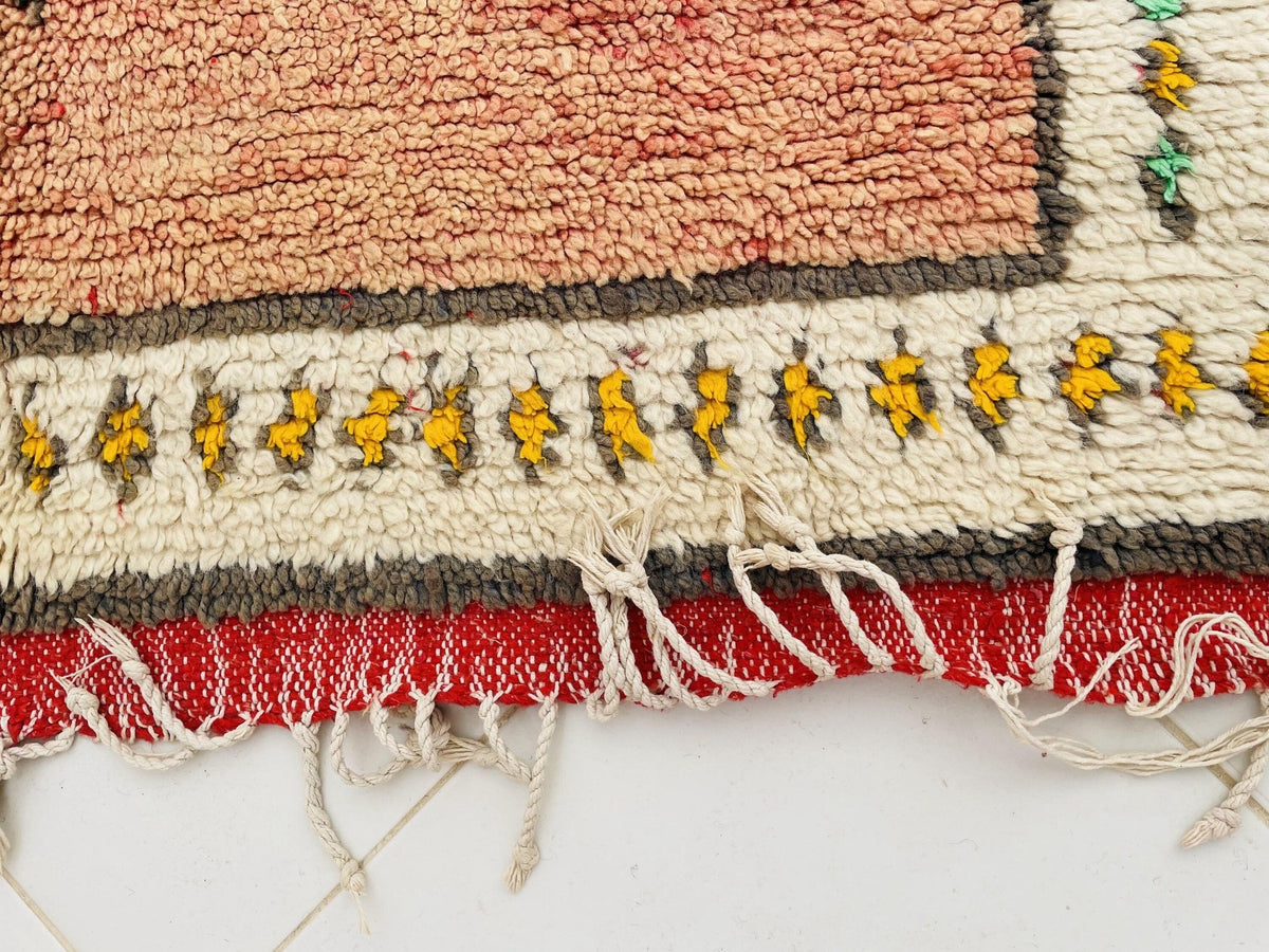 Detail image of an orange Moroccan rug with fringed edges and a decorative border.