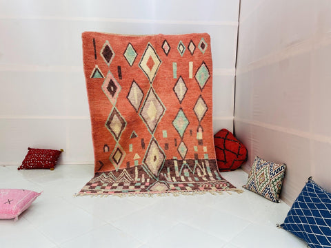 Lifestyle shot of an orange and green Moroccan rug with geometric patterns in a studio setting.