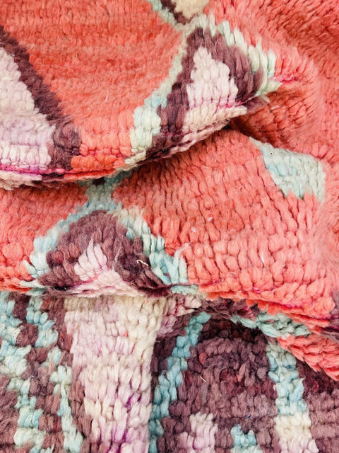 Lifestyle view of a pink and blue Moroccan rug featuring geometric patterns in a studio environment.