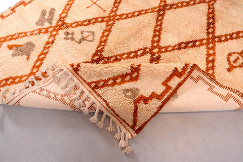 Detail close-up of a beige and brown Beni Ourain rug with a diamond design and fringe edge.