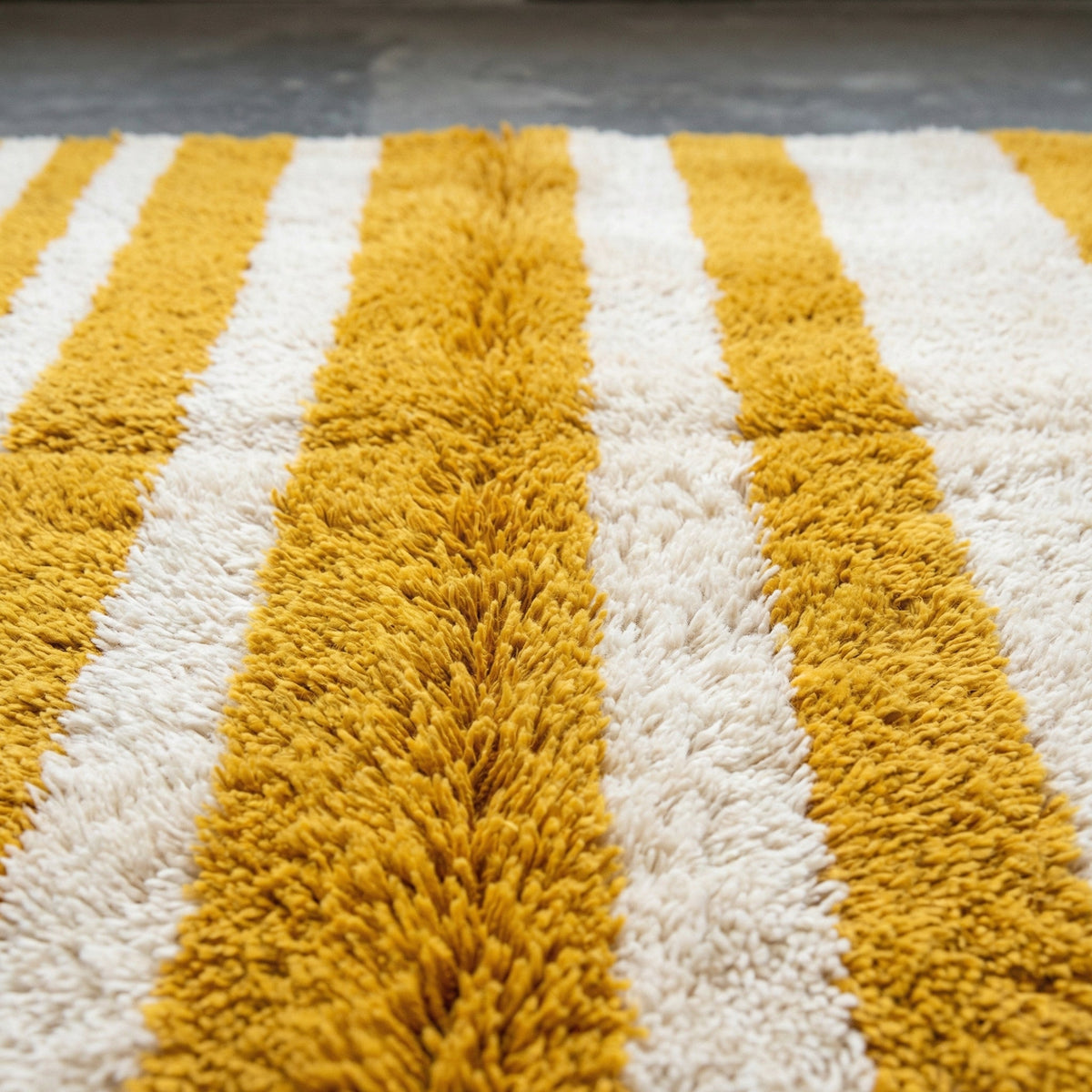 Detail shot of the plush texture and striped pattern of a mustard rug.