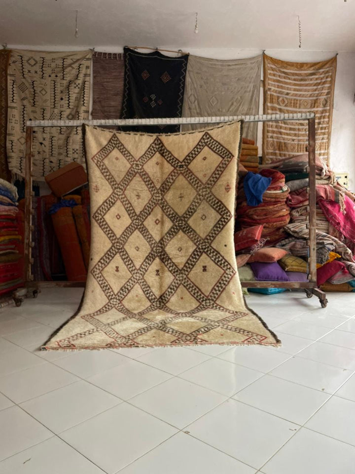 Lifestyle shot of a vintage Moroccan rug featuring geometric patterns in beige and brown.
