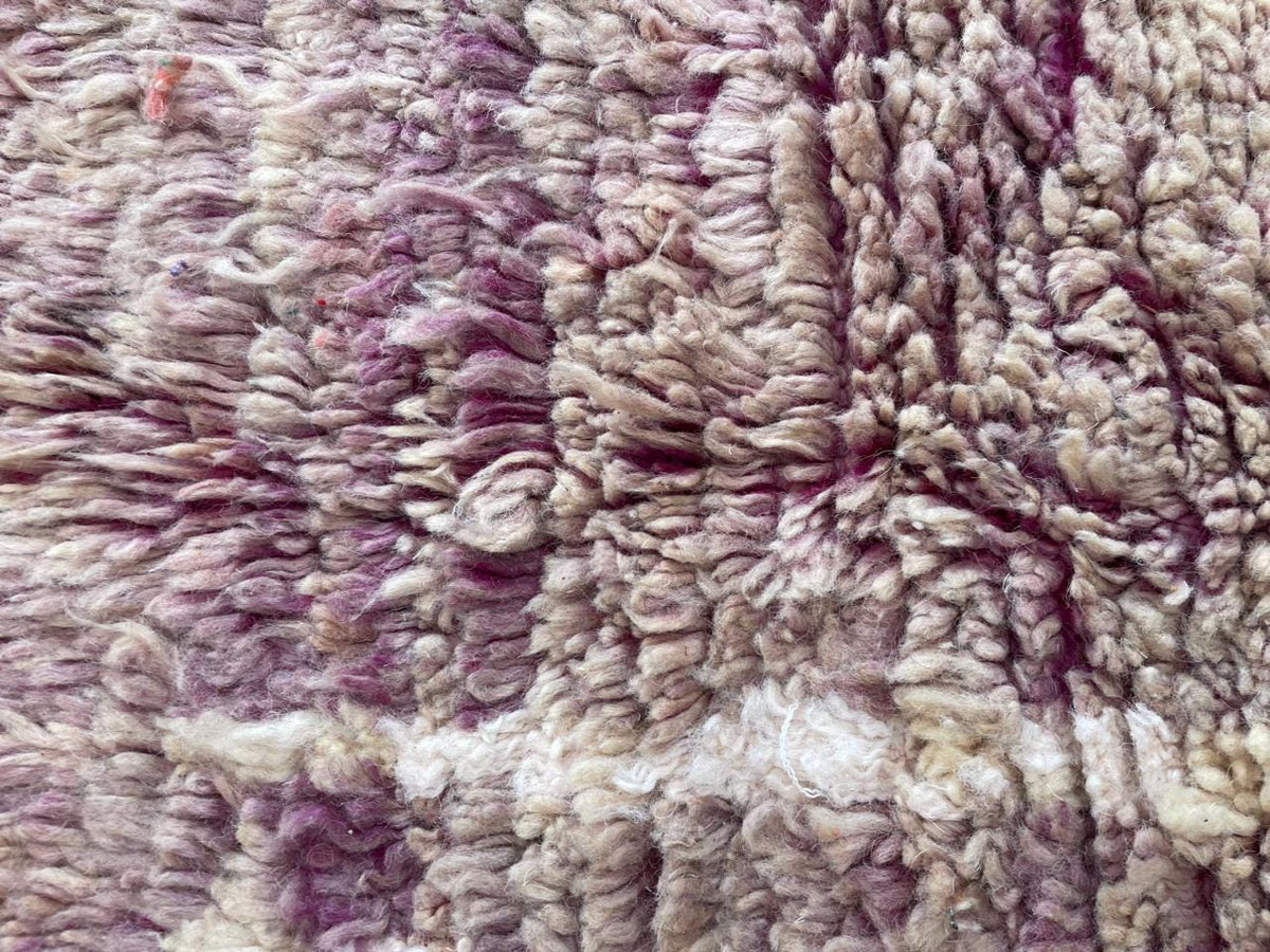Detail shot of a vintage Moroccan rug featuring tribal patterns in purple and cream colors.
