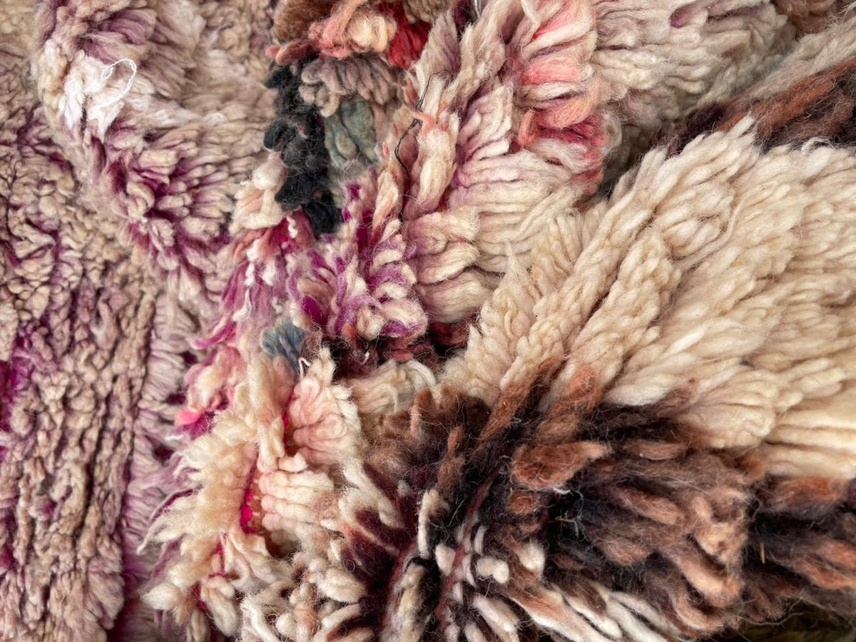 Detail shot of a vintage Moroccan rug with textured surface and tribal designs in brown and red.