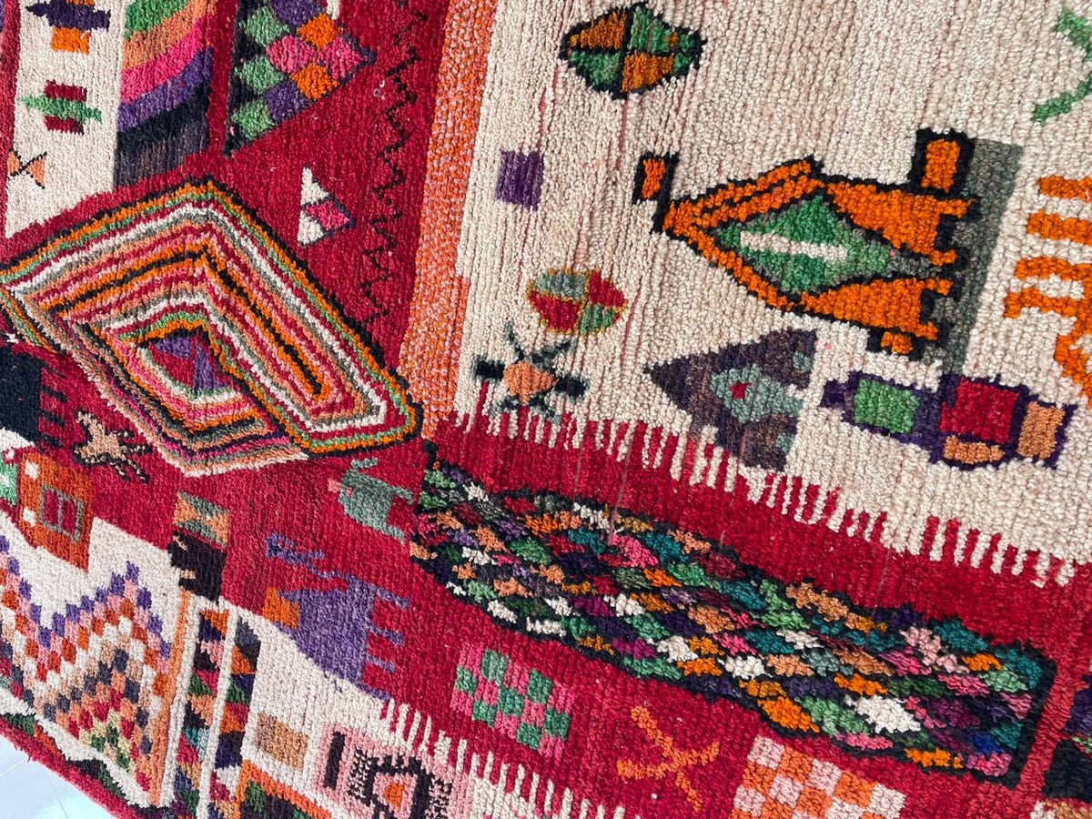 Detail close-up of a vintage Moroccan rug displaying colorful motifs in red, cream, and orange.